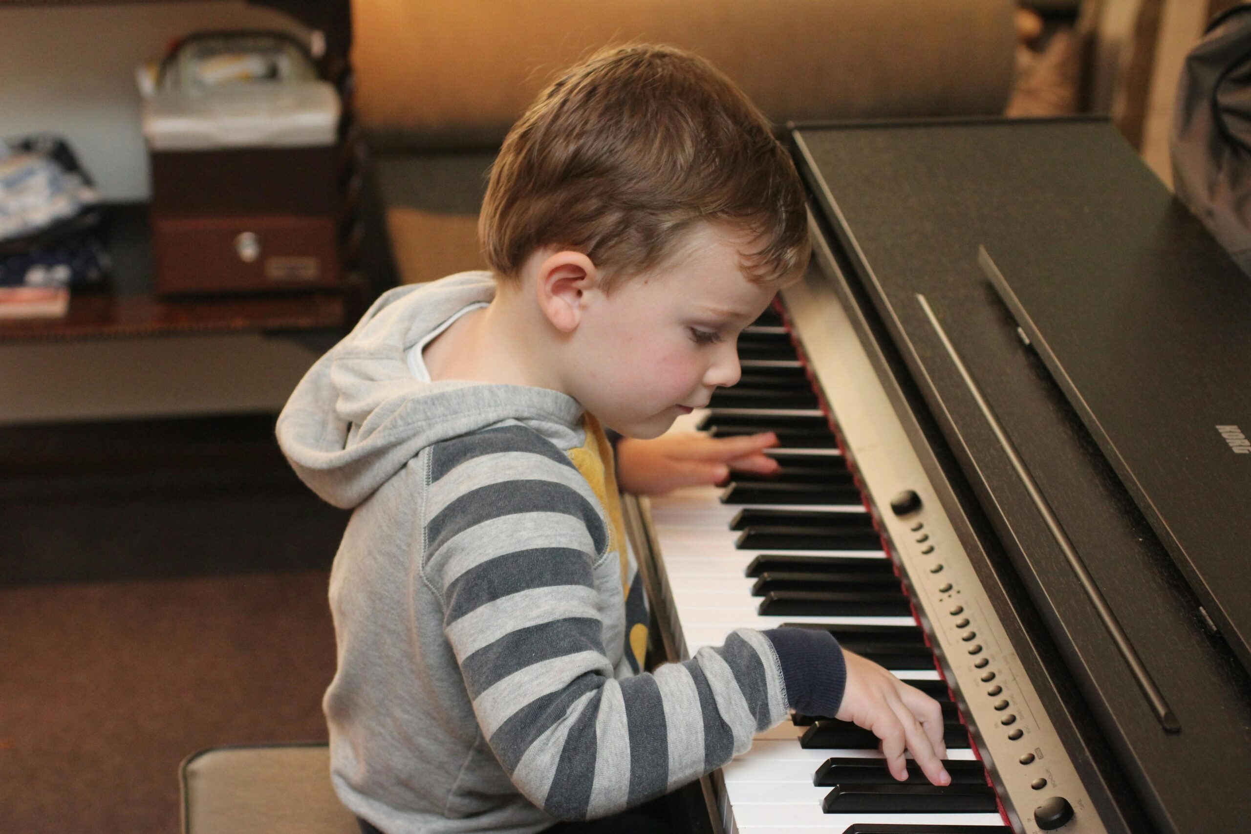 A young child focuses intently on playing the piano in a cozy room setting.