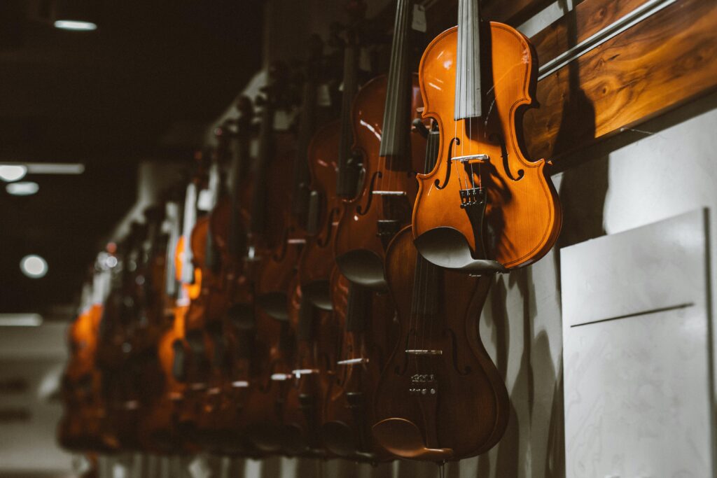 Row of violins hanging on a wall in a music store, showcasing string instruments.